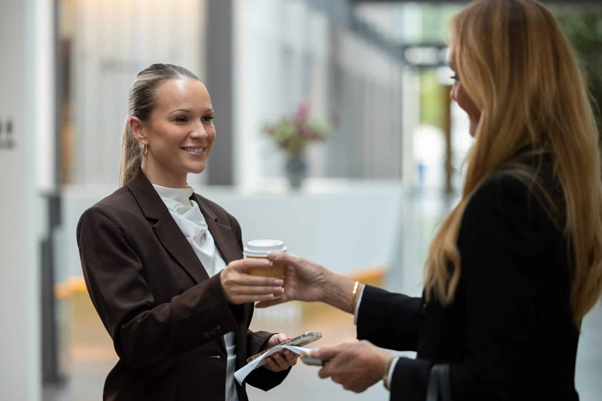 To kvinder udveksler en kaffekop under en samtale